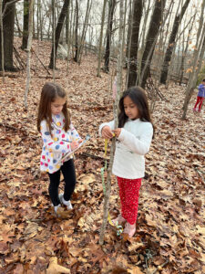 Two young kindergarten girls measuring a sapling in the woods and taking notes