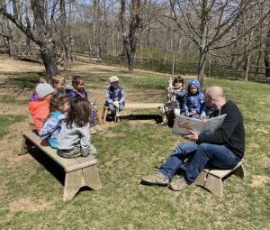 A father reading to a circle of children outdoors