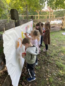 Children painting a long roll of paper pinned up to a fence