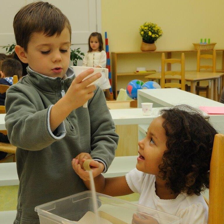 Preschool children playing with sand and a funnel in a Montessori classroom